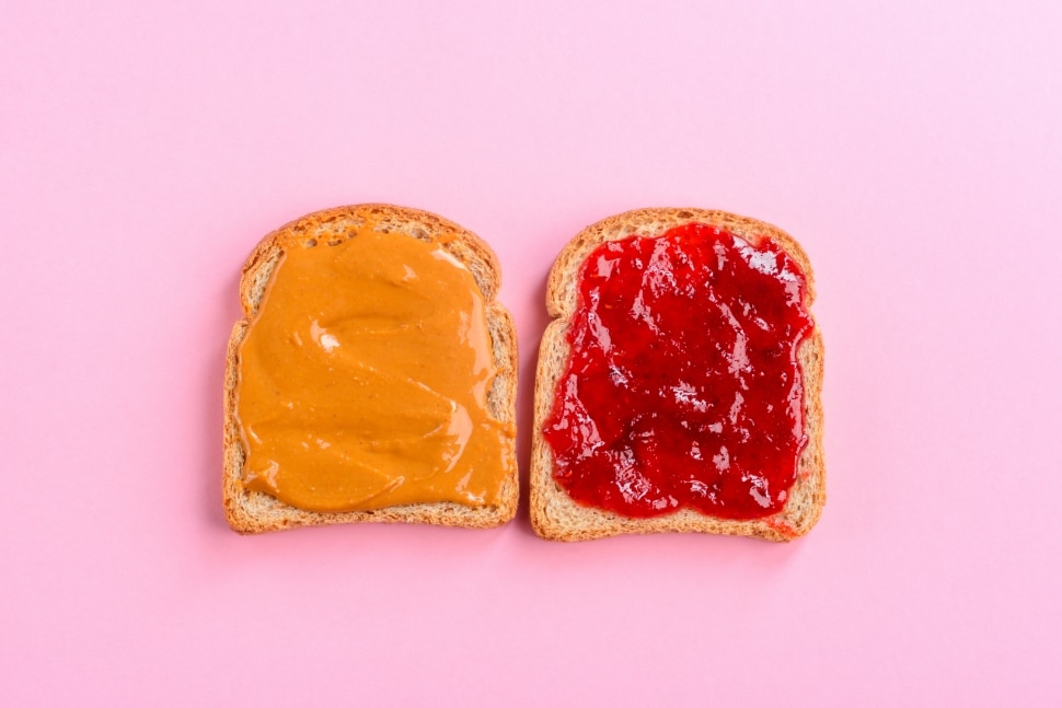 peanut butter and jelly on open slices of bread with pink background